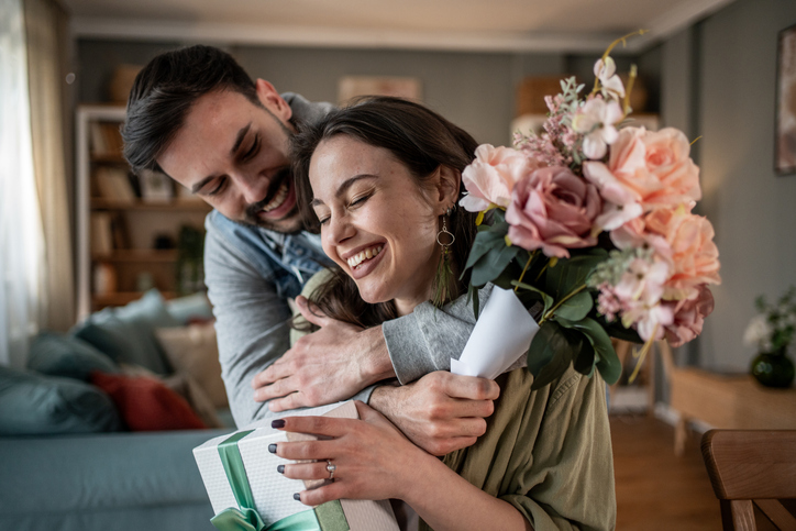Ein junger Mann umarmt seine Freundin und schenkt ihr einen Blumenstrauß