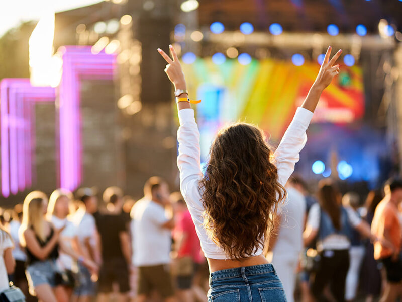 Eine junge Frau tanzt mit erhobenen Händen vor einer Open-Air Bühne
